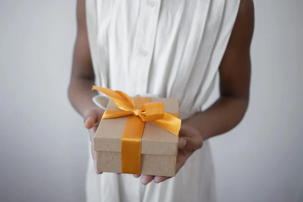 Ragazza che tiene tra le mani un pacchetto regalo fasciato con un nastro arancione.
